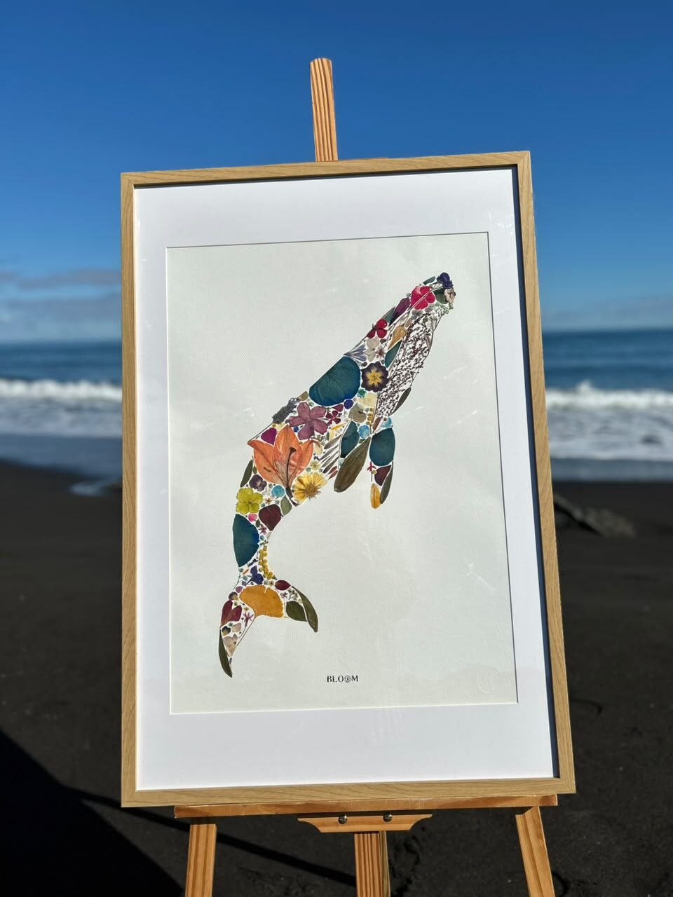 Cuadro de ballena hecha con flores prensadas, sobre caballete en la playa