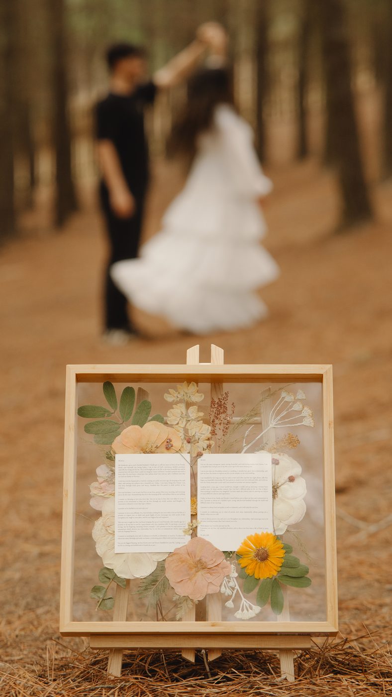 Cuadro con la invitación de matrimonio y flores prensadas, con los novios de fondo
