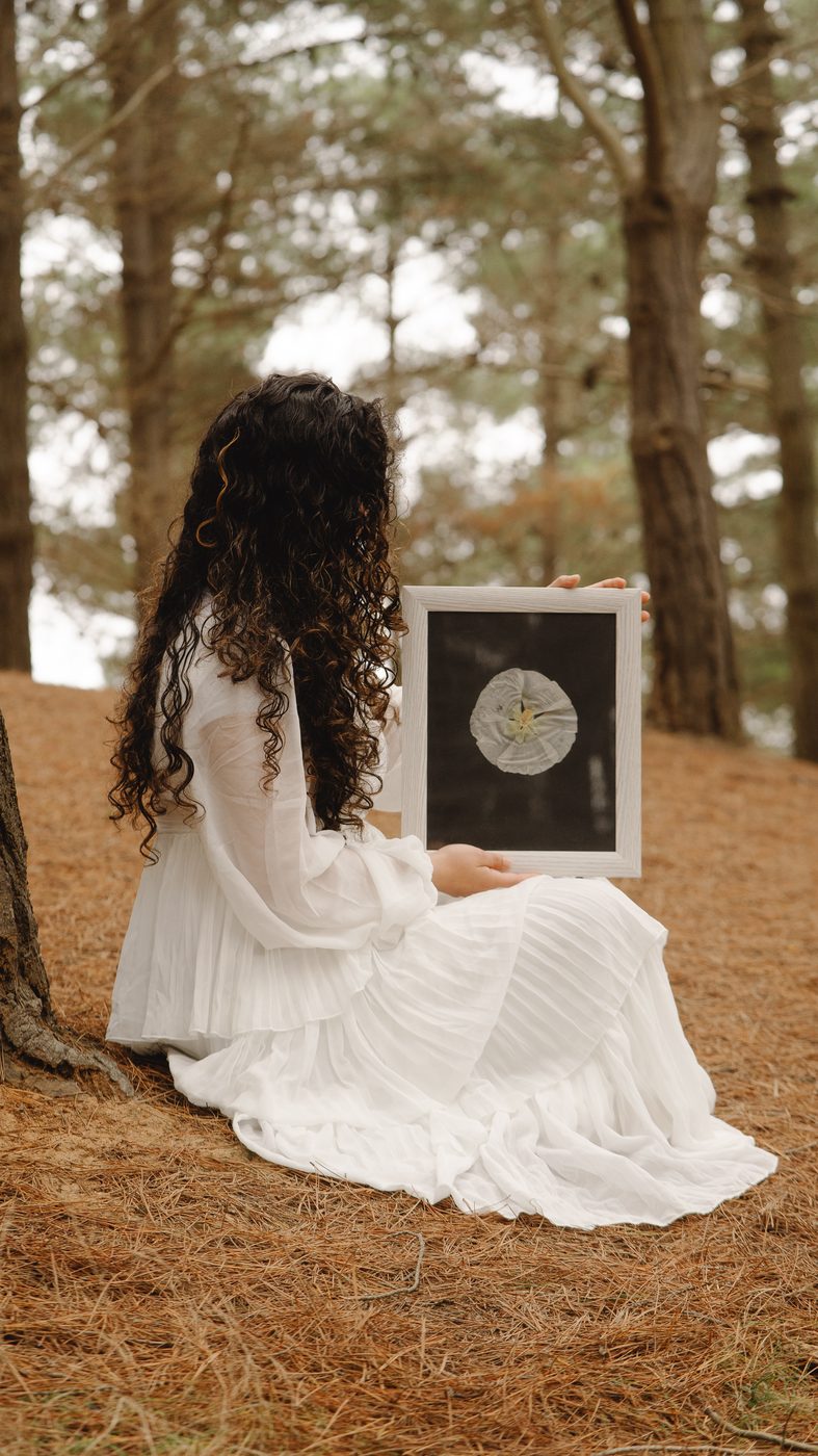 Mujer en el bosque sosteniendo un cuadro de flores prensadas