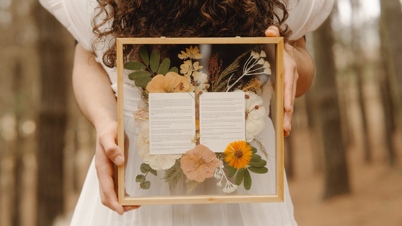 Marco abierto con la invitación de matrimonio y flores prensadas